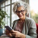 Healthy cheerful senior female using smart phone in her cozy living room, technology and communication